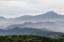 Sebuah kafe modern dengan jendela besar menghadap pegunungan hijau dan langit biru yang cerah di Sentul, menawarkan suasana tenang untuk bersantai. Pengunjung dapat menikmati kopi hangat sambil memandangi pemandangan alam yang menyejukkan.