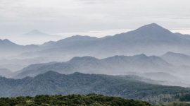 Sebuah kafe modern dengan jendela besar menghadap pegunungan hijau dan langit biru yang cerah di Sentul, menawarkan suasana tenang untuk bersantai. Pengunjung dapat menikmati kopi hangat sambil memandangi pemandangan alam yang menyejukkan.