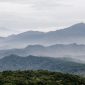 Sebuah kafe modern dengan jendela besar menghadap pegunungan hijau dan langit biru yang cerah di Sentul, menawarkan suasana tenang untuk bersantai. Pengunjung dapat menikmati kopi hangat sambil memandangi pemandangan alam yang menyejukkan.