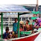 Keluarga dengan dua anak kecil sedang bermain di tepi pantai berpasir putih, menikmati momen kebersamaan di destinasi liburan tropis. Mereka terlihat bahagia dengan latar belakang laut biru jernih dan pohon kelapa yang melambai.