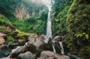 Seorang wisatawan tengah menikmati keindahan Curug Cilember, salah satu air terjun bertingkat di Bogor, dengan latar belakang hutan tropis yang rimbun dan asri. Suasana tenang di tengah gemericik air memberikan pengalaman relaksasi yang mendalam.