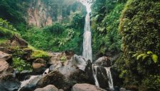 Seorang wisatawan tengah menikmati keindahan Curug Cilember, salah satu air terjun bertingkat di Bogor, dengan latar belakang hutan tropis yang rimbun dan asri. Suasana tenang di tengah gemericik air memberikan pengalaman relaksasi yang mendalam.