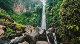Seorang wisatawan tengah menikmati keindahan Curug Cilember, salah satu air terjun bertingkat di Bogor, dengan latar belakang hutan tropis yang rimbun dan asri. Suasana tenang di tengah gemericik air memberikan pengalaman relaksasi yang mendalam.