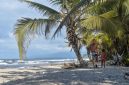 Sebuah keluarga sedang menikmati keindahan pantai berpasir putih di Sumbawa yang dihiasi dengan perbukitan hijau, menciptakan suasana liburan yang damai dan menyegarkan. Anak-anak tampak bermain air di tepi pantai, sementara orang dewasa bersantai menikmati panorama alam yang masih sangat asri.