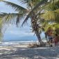 Sebuah keluarga sedang menikmati keindahan pantai berpasir putih di Sumbawa yang dihiasi dengan perbukitan hijau, menciptakan suasana liburan yang damai dan menyegarkan. Anak-anak tampak bermain air di tepi pantai, sementara orang dewasa bersantai menikmati panorama alam yang masih sangat asri.