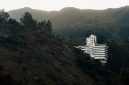 Pemandangan hotel modern dengan kolam renang yang dikelilingi pepohonan hijau rindang di kawasan Puncak, Bogor. Suasana tenang ini cocok untuk relaksasi dan melarikan diri dari hiruk pikuk perkotaan.