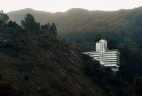 Pemandangan hotel modern dengan kolam renang yang dikelilingi pepohonan hijau rindang di kawasan Puncak, Bogor. Suasana tenang ini cocok untuk relaksasi dan melarikan diri dari hiruk pikuk perkotaan.